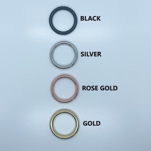 May include: Four metal rings in different colors: black, silver, rose gold, and gold. The rings are arranged vertically, with the black ring at the top and the gold ring at the bottom.