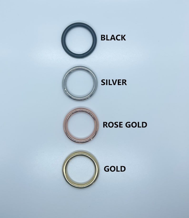 May include: Four metal rings in different colors: black, silver, rose gold, and gold. The rings are arranged vertically, with the black ring at the top and the gold ring at the bottom.