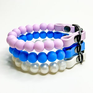 A stack of breakaway bead cat collars made with lilac, light blue, pearl silicone beads paired with lilac, light blue and white biothane.