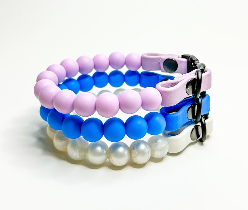 A stack of breakaway bead cat collars made with lilac, light blue, pearl silicone beads paired with lilac, light blue and white biothane.