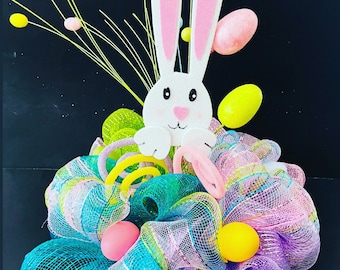 May include: A pastel Easter wreath with a white bunny cutout, pink and yellow Easter eggs, and green and purple mesh.