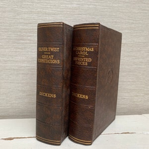 May include: Two antique books with brown leather covers. The titles "Oliver Twist Great Expectations" and "A Christmas Carol Reprinted Pieces" are embossed in gold lettering. The author's name, Dickens, is also in gold. The books have gold trim.