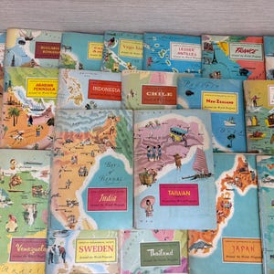 May include: A collection of vintage Around the World Program booklets featuring colorful illustrated maps of various countries including India, Taiwan, Japan, and Russia. Each booklet displays regional landmarks, cultural icons, and text labels.