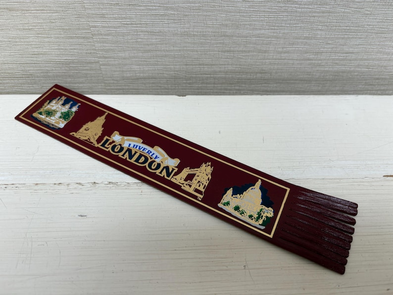 May include: A burgundy bookmark with gold accents and the word "LONDON" in white. The bookmark features illustrations of London landmarks. The bottom edge has a fringed design.