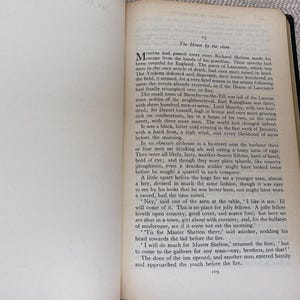 May include: Open book with text on aged paper. The text is in English, with the title "The House by the shore" at the top of the page. The pages are yellowed with age, and the binding is black.