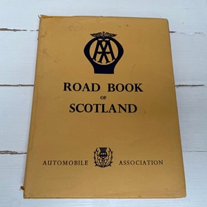 May include: A vintage Road Book of Scotland, with the Automobile Association logo and a thistle emblem on the cover. The cover is a faded yellow with black text. The book's title is clearly visible.