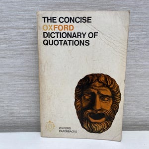 Könnte beinhalten: Der Einband des Buches "The Concise Oxford Dictionary of Quotations" zeigt eine braune und schwarze Illustration einer theatralischen Maske mit einem ernsten Ausdruck. Der Buchtitel ist in schwarzer Schrift gedruckt, wobei das Wort "Oxford" orange ist.