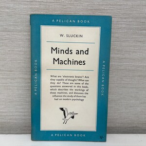 Op de afbeelding: Een vintage Pelican boek getiteld Minds and Machines door W. Sluckin. De kaft is blauwgroen met een wit middenpaneel met zwarte tekst en een kleine illustratie van een pelikaan. De tekst beschrijft de studie naar elektronische hersenen.