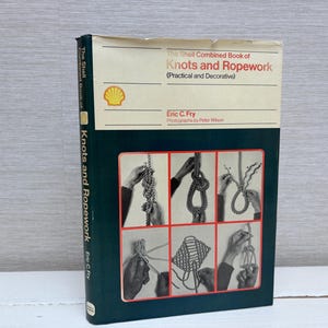 May include: A vintage book titled "The Shell Combined Book of Knots and Ropework" by Eric C. Fry. The cover is dark green with a cream-colored top section. The book features illustrations of knot tying techniques.