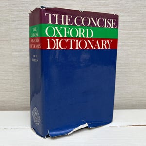 Peut inclure: Un exemplaire du "Concise Oxford Dictionary, cinquième édition". Le livre a une couverture bleue avec une bande rouge, verte et violette en haut. Le titre est imprimé en blanc.