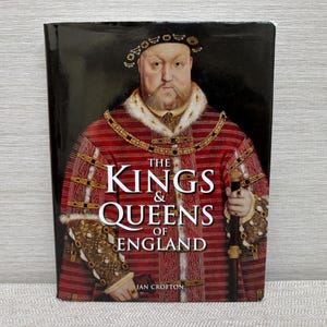 May include: A hardcover book titled "The Kings & Queens of England" featuring a portrait of a historical figure in a red and gold patterned robe. The book cover has a black background and the author's name is "Ian Crofton."
