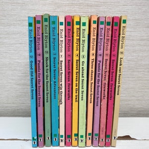 Peut inclure: Une collection de 14 livres brochés aux couvertures colorées, tous portant le titre "Secret Seven" et l'auteur "Enid Blyton". Les livres sont disposés verticalement, avec les dos face au spectateur.