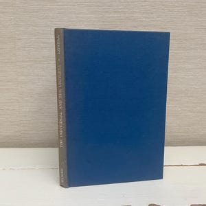 Pode incluir: Um livro encadernado em azul com o título "The Individual and the Universe" de John A. Passmore.