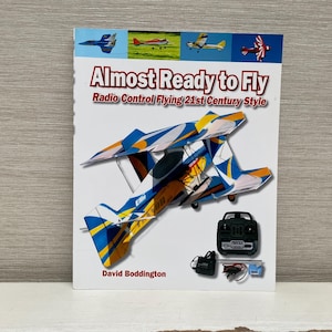 May include: Book cover with the title "Almost Ready to Fly: Radio Control Flying 21st Century Style" by David Boddington. The cover features a blue and yellow biplane with a black and white radio control transmitter.