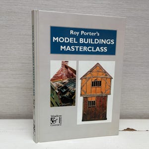 Op de afbeelding: Een boek getiteld "Roy Porter's Model Buildings Masterclass" van Windrow & Greene. De omslag toont twee modelgebouwen, een met een rode bakstenen buitenkant en de andere met een houten frame.