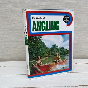 Könnte beinhalten: Ein Vintage-Buch mit dem Titel "The World of Angling" mit einem roten, weißen und blauen Einband. Der Einband zeigt ein Foto von zwei Personen, die von einem Boot aus auf einem Fluss angeln.