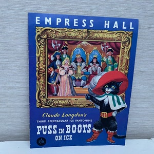 Puede incluir: Un cartel vintage que anuncia la tercera pantomima de hielo espectacular de Claude Langdon, "Puss in Boots on Ice", en el Empress Hall. El cartel presenta una ilustración colorida de Puss in Boots con un sombrero rojo y una capa verde, de pie frente a una escena que representa una corte real.