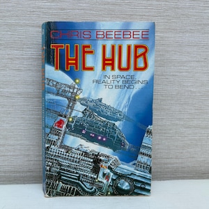 Op de afbeelding: Een sciencefiction paperback roman getiteld "The Hub" van Chris Beebee. De omslag toont een kleurrijke illustratie van een futuristisch ruimtestation met de tekst "In de ruimte begint de realiteit te buigen..."