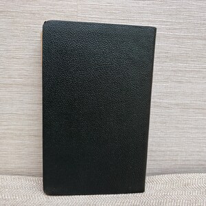 May include: A black, rectangular object with a textured surface. The object is upright and appears to be made of leather or a similar material. The edges are slightly rounded. The background is a light wood grain.