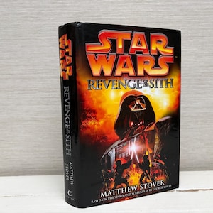 May include: A hardback book titled "Star Wars: Revenge of the Sith" is shown. The cover depicts Darth Vader against a fiery backdrop. The author's name, Matthew Stover, is also visible.