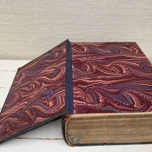 May include: A large, antique book with a marbled cover in shades of brown, blue, and pink. The book is open, revealing a plain, brown interior.