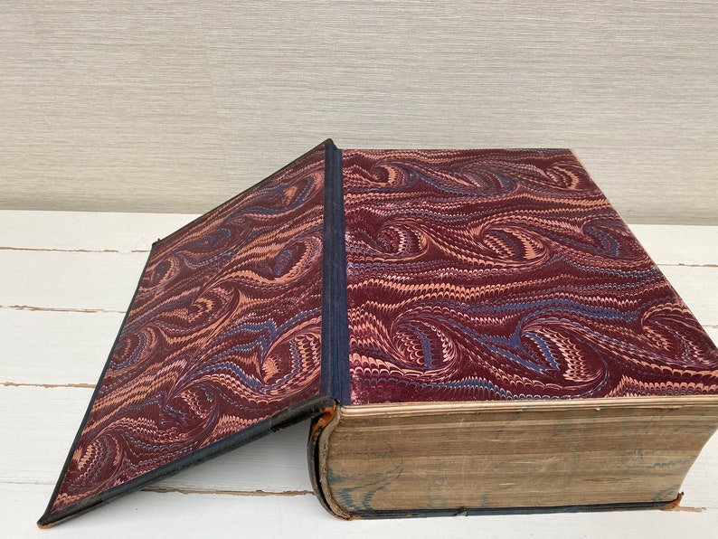 May include: A large, antique book with a marbled cover in shades of brown, blue, and pink. The book is open, revealing a plain, brown interior.