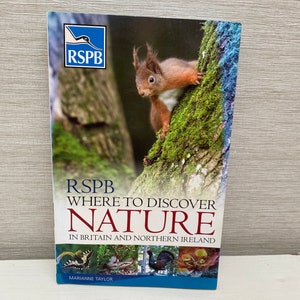 Może przedstawiać: Okładka książki z rudym wiewiórką na pniu drzewa. Tytuł książki to "RSPB Where to Discover Nature in Britain and Northern Ireland" autorstwa Marianne Taylor. Okładka zawiera również niebieskie logo z literami RSPB.