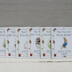 May include: A collection of children's books by Beatrix Potter, featuring titles like "The Tale of Peter Rabbit." The books have white covers with illustrations and text, including the author's name. The spines are visible, and the books are arranged side by side.