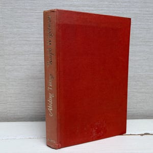 May include: A red hardcover book with the title "Abiding Ture" and the author's name, "Kaipo Wegelman," in gold lettering on the spine. The book is positioned upright against a light grey backdrop.