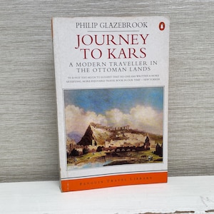 Op de afbeelding: Een vintage paperback boek getiteld "Journey to Kars: A Modern Traveller in the Ottoman Lands" door Philip Glazebrook. De omslag toont een schilderij van een landschap met een stad in de verte.