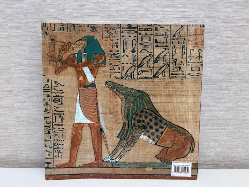 May include: An Egyptian papyrus print featuring a detailed illustration of a figure with a bird head and a jackal-headed deity. The artwork is rendered in earthy tones of brown, beige, and teal, with hieroglyphs along the borders.