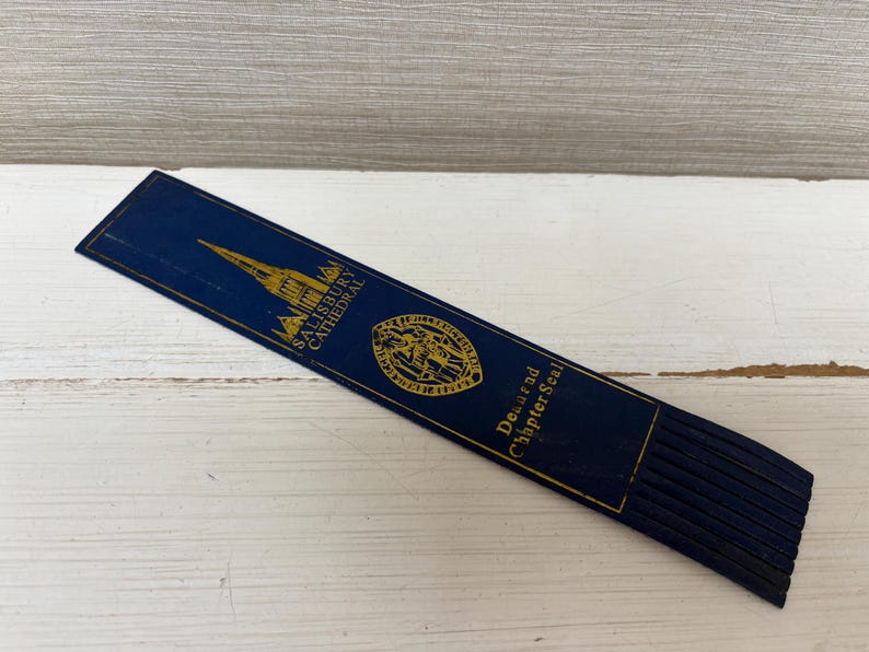 May include: A navy blue bookmark with gold lettering and a gold illustration of a cathedral. The bookmark has the text "Salisbury Cathedral" and "Dean and Chapter Seal". The bottom edge has several navy blue tassels.