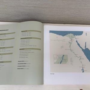 May include: An open book displays a page with a historical chronology and a map of ancient Egypt. The map features blue water and green land, with text indicating locations and periods. The opposite page lists historical periods.