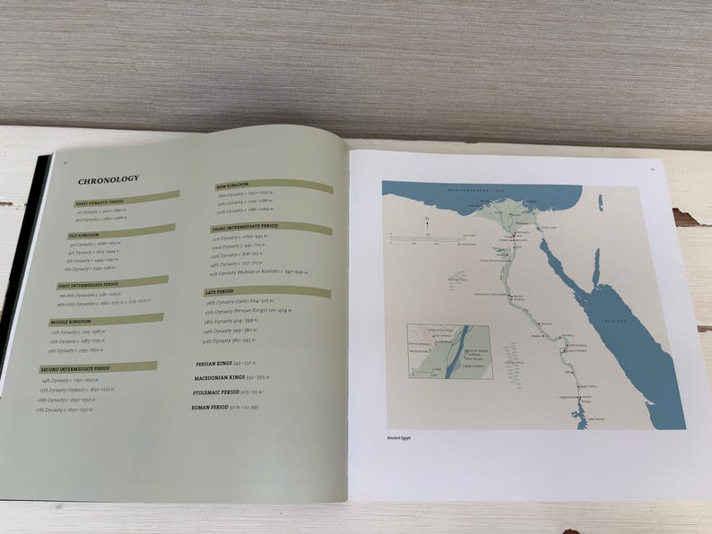 May include: An open book displays a page with a historical chronology and a map of ancient Egypt. The map features blue water and green land, with text indicating locations and periods. The opposite page lists historical periods.