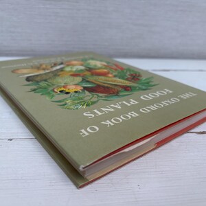 May include: The Oxford Book of Food Plants. A vintage book with a green cover featuring a colorful illustration of various fruits and vegetables. The book's title is printed in white.