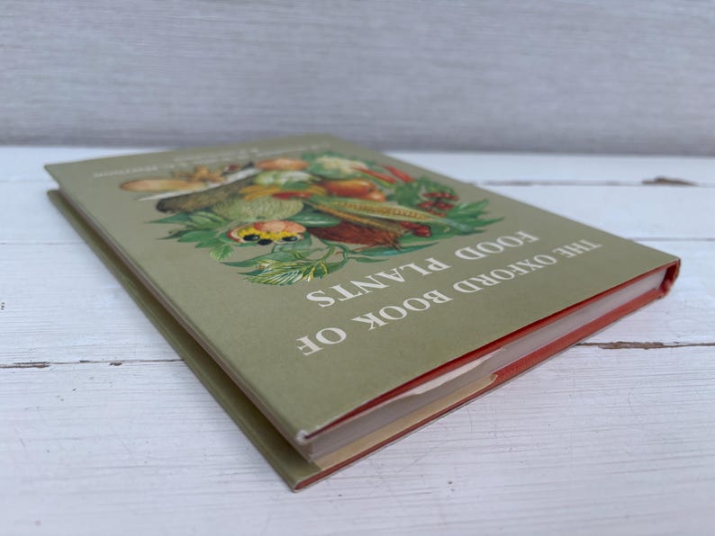 May include: The Oxford Book of Food Plants. A vintage book with a green cover featuring a colorful illustration of various fruits and vegetables. The book's title is printed in white.