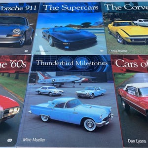 Puede incluir: Una colección de libros de coches clásicos con un avión a reacción rojo, blanco y azul, un Porsche 911 plateado, un supercoche negro, un Corvette amarillo, un Ford Thunderbird rojo, un Ford Thunderbird azul y un Ford Mustang rojo. Los títulos de los libros son "The Porsche 911", "The Supercars", "The Corvette", "Cars of the '60s", "Thunderbird Milestones" y "Cars of the".