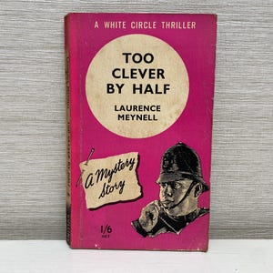 以下が含まれることがあります： ローレンス・メイネル著のピンク色のペーパーバック「Too Clever By Half」。この本はホワイトサークル・スリラーであり、ミステリー小説です。表紙には、警官帽をかぶった男性の白黒のイラストが描かれています。