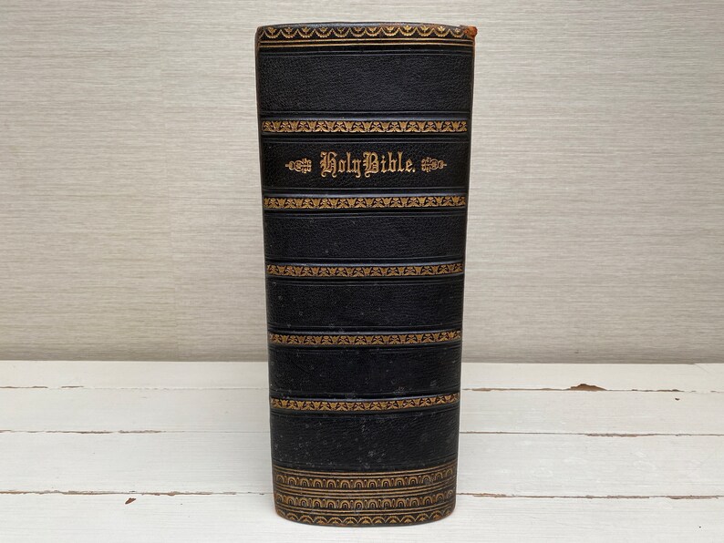 May include: A black leather-bound book with gold lettering that reads "Holy Bible". The book has a decorative pattern of gold lines and designs.