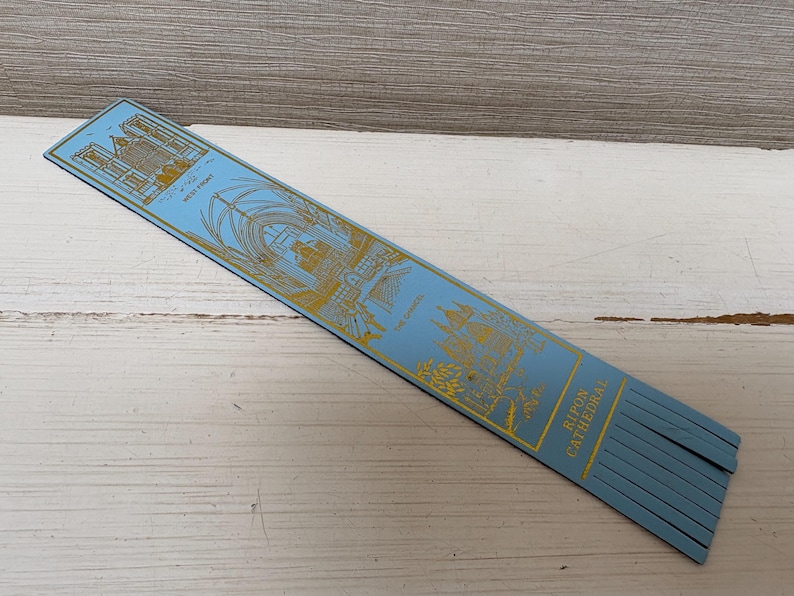May include: A light blue bookmark with gold illustrations of a cathedral. The bookmark has the words "West Front" and "Ripon Cathedral" printed on it. The bottom of the bookmark has a fringe.