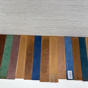 May include: A collection of leather bookmarks in various colors, including brown, green, blue, and tan. Each bookmark has a fringed bottom and a rectangular shape. Some have a textured appearance, and one has a barcode sticker.