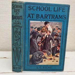 Pode incluir: Livro antigo intitulado "School Life at Bartram's" por L.C. Silke. A capa azul apresenta o título e uma ilustração de alunos. A lombada mostra o título e o nome do autor em preto sobre fundo azul.