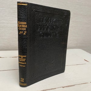 以下が含まれることがあります： 金色の文字で「Hawkins Electrical Guide No. 2」と書かれた黒い革装丁の本。ダイナモ、モーター、機器、試験の管理について書かれています。