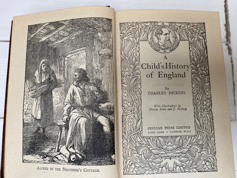 May include: Open book with illustrations. The left page shows a black and white drawing of a man and woman in a cottage. The right page has the title "A Child's History of England" by Charles Dickens, with illustrations by Marcus Stone and J. Mabury.