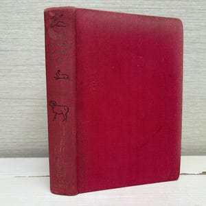 May include: A vintage, red hardcover book with embossed illustrations of a bird, rabbit, and ram on the spine. The book has a textured cover and is set against a neutral background. The book's title is partially visible.