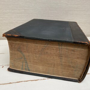 May include: A vintage, leather-bound book with a dark blue cover and a faded, patterned spine. The book is closed and lying on a white surface.