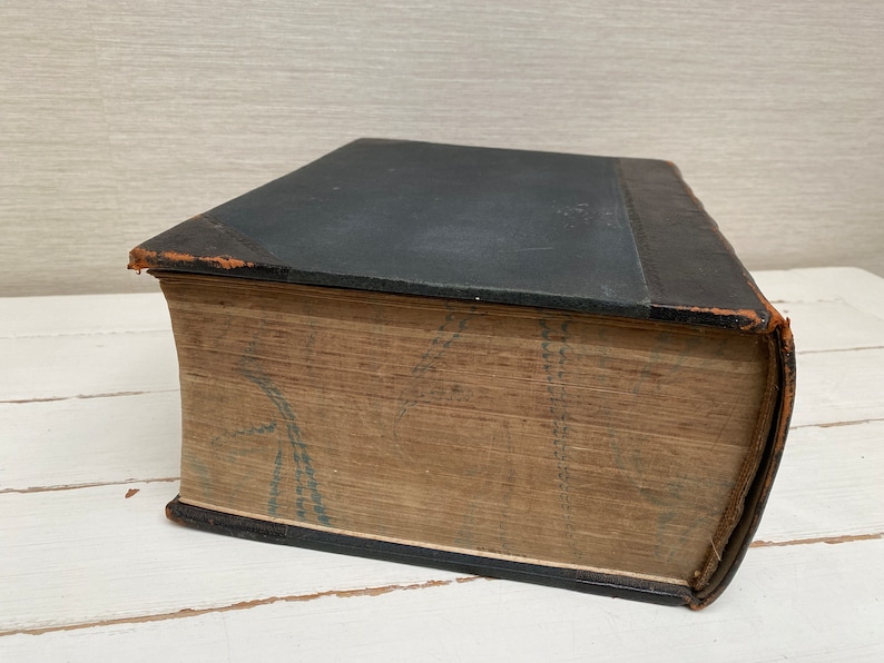 May include: A vintage, leather-bound book with a dark blue cover and a faded, patterned spine. The book is closed and lying on a white surface.