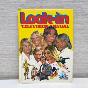 Peut inclure: Un livre jaune intitulé "Look-in Television Annual" représentant un groupe de personnes, dont un robot, Mickey Mouse et un joueur de football. Le texte sous le titre indique "Top TV Action + Pop Comedy Sport and Lots More!"
