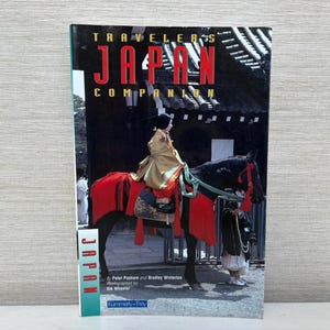 May include: A book titled "Travelers Japan Companion" featuring a photograph of a person in traditional Japanese clothing riding a horse. The cover displays the word "JAPAN" in large red letters.