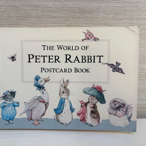 May include: A postcard book titled "The World of Peter Rabbit." The cover features illustrations of characters from the story, including a rabbit, duck, and hedgehog. The book has a light blue border and is decorated with small drawings of a bee and birds.